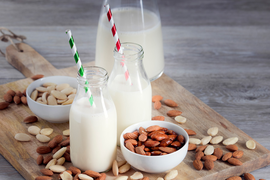 Rezept alkoholfreier Mandelcocktail Stimmungsbild "alkoholfreier Mandelcocktail": zwei gefüllte Weithalsflaschen mit bunten Strohhalmen stehen auf einem Holzbrett mit Mandeln