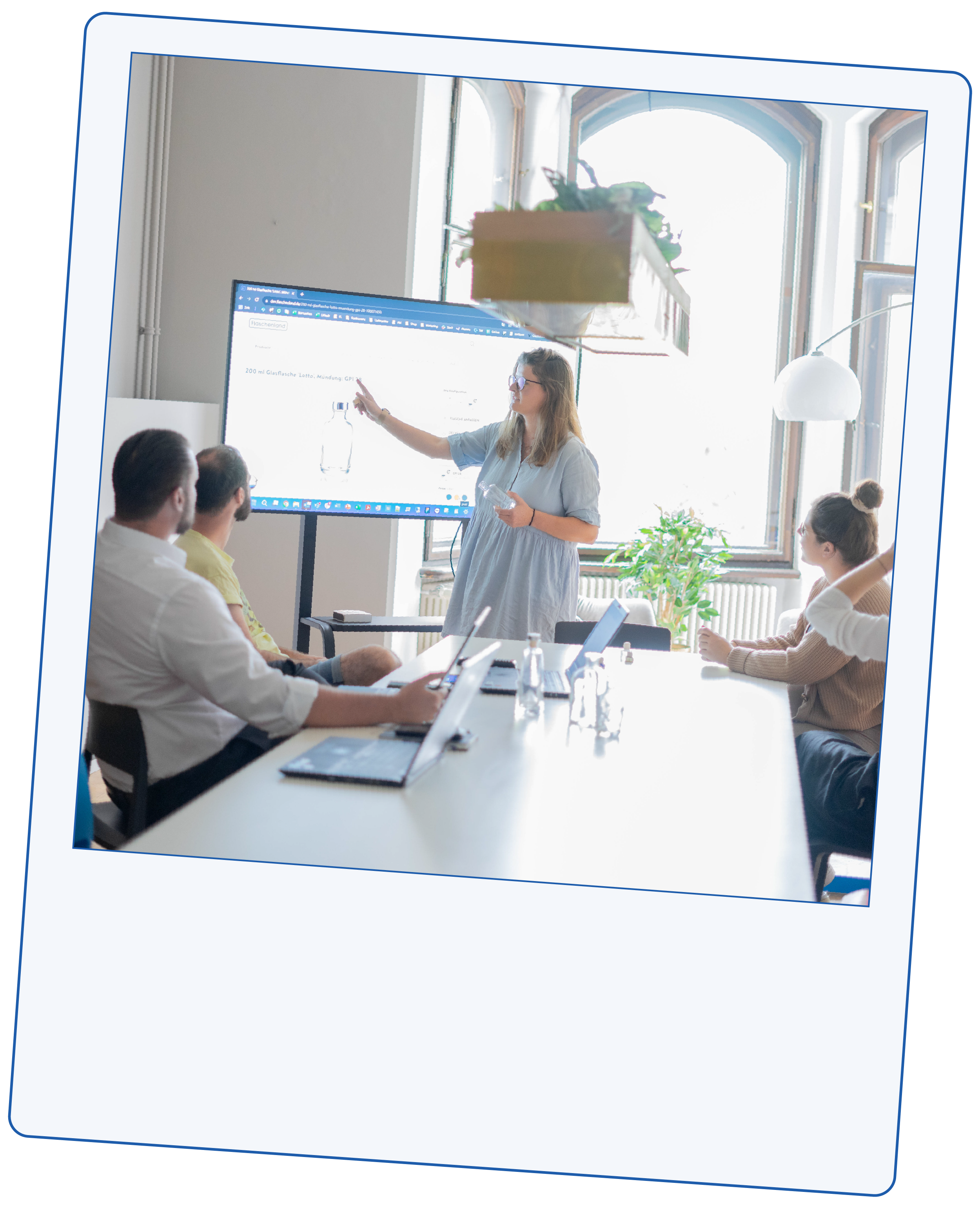 Meeting Stimmungsbild: Fünf Personen sind in einem Meeting, eine Frau erklärt etwas an einem Bildschirm