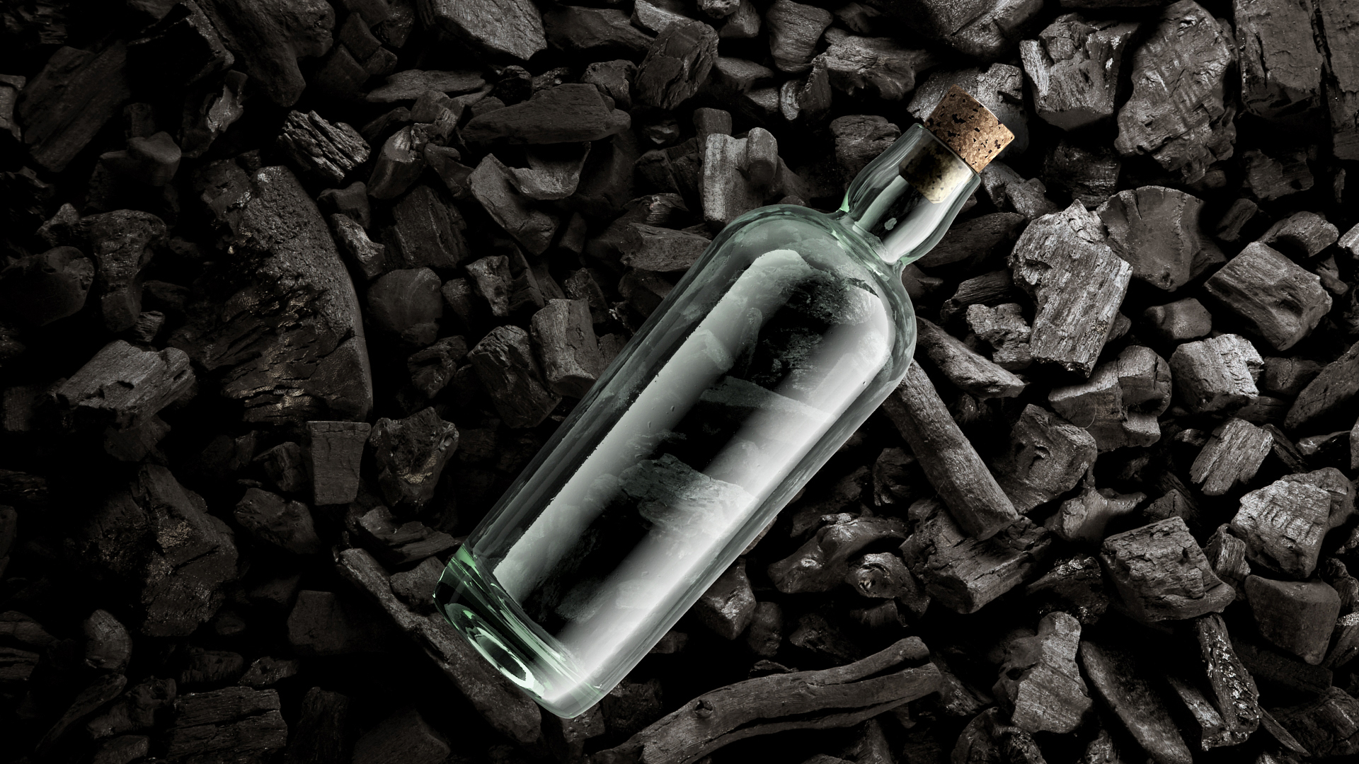 Estal Corkcoal Verschlüsse Stimmungsbild: eine transparente Glasflasche der Marke Estal mit Corkcoal-Verschluss liegt auf einem Untergrund aus Kohlestücken