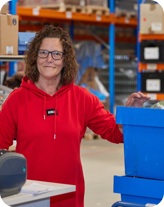 Vorarbeiterin Verpackungslogistik Freundliche Frau in rotem Pullover steht in einem Lager mit Gläsern und Flaschen
