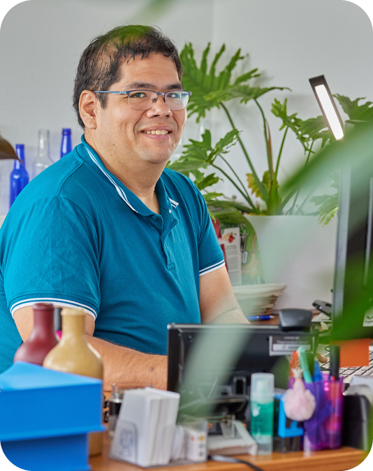 Lächelnder Mann mit blauem Oberteil sitzt am Schreibtisch