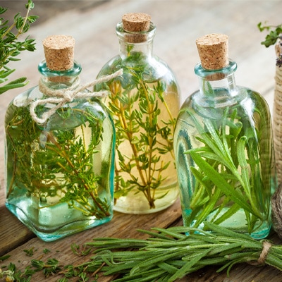 Drei Klarglasflaschen gefüllt mit aromatisiertem Öl, verschlossen mit einem Korken