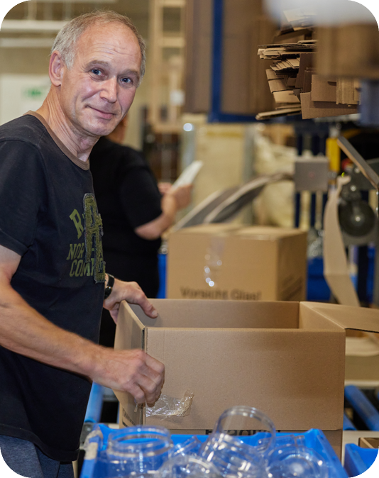 Mitarbeiter Verpackung Freundlicher Mann in schwarzem T-Shirt verpackt Einmachgläser in Versandkartons