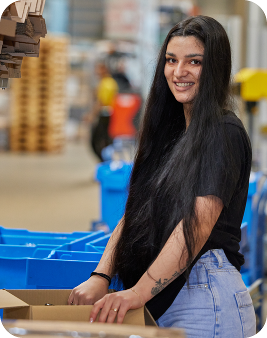 Mitarbeiterin Verpackungslogistik Junge Frau in schwarzem T-Shirt packt einen Karton in der Logistik