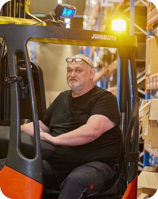 Mitarbeiter Lager Mann in schwarzer Kleidung sitzt in einem Gabelstapler in einem Versandlager