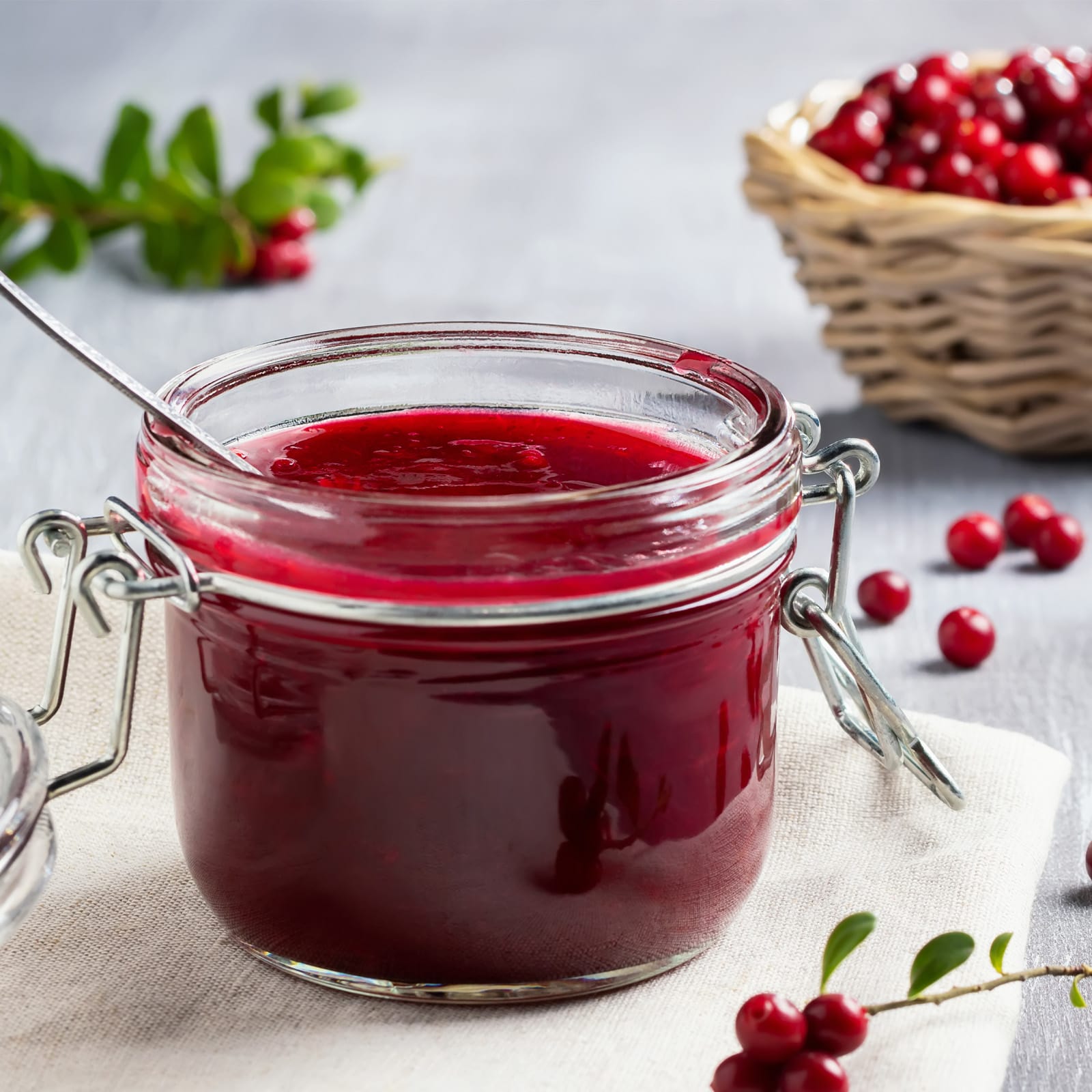 Kleines Drahtbügelglas gefüllt mit roter hausgemachter Marmelade, arrangiert auf einer Stoffserviette mit roten Beeren